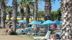 Ein Strandbereich mit Palmen, Liegestühlen und blauen Sonnenschirmen.