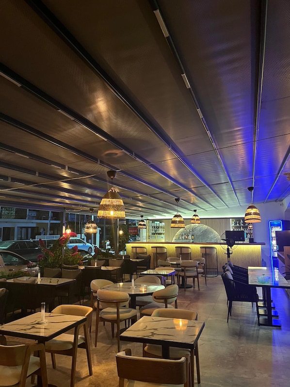 Un restaurante interior con mesas y sillas, una zona de bar y un techo con diseño de cuadrícula.