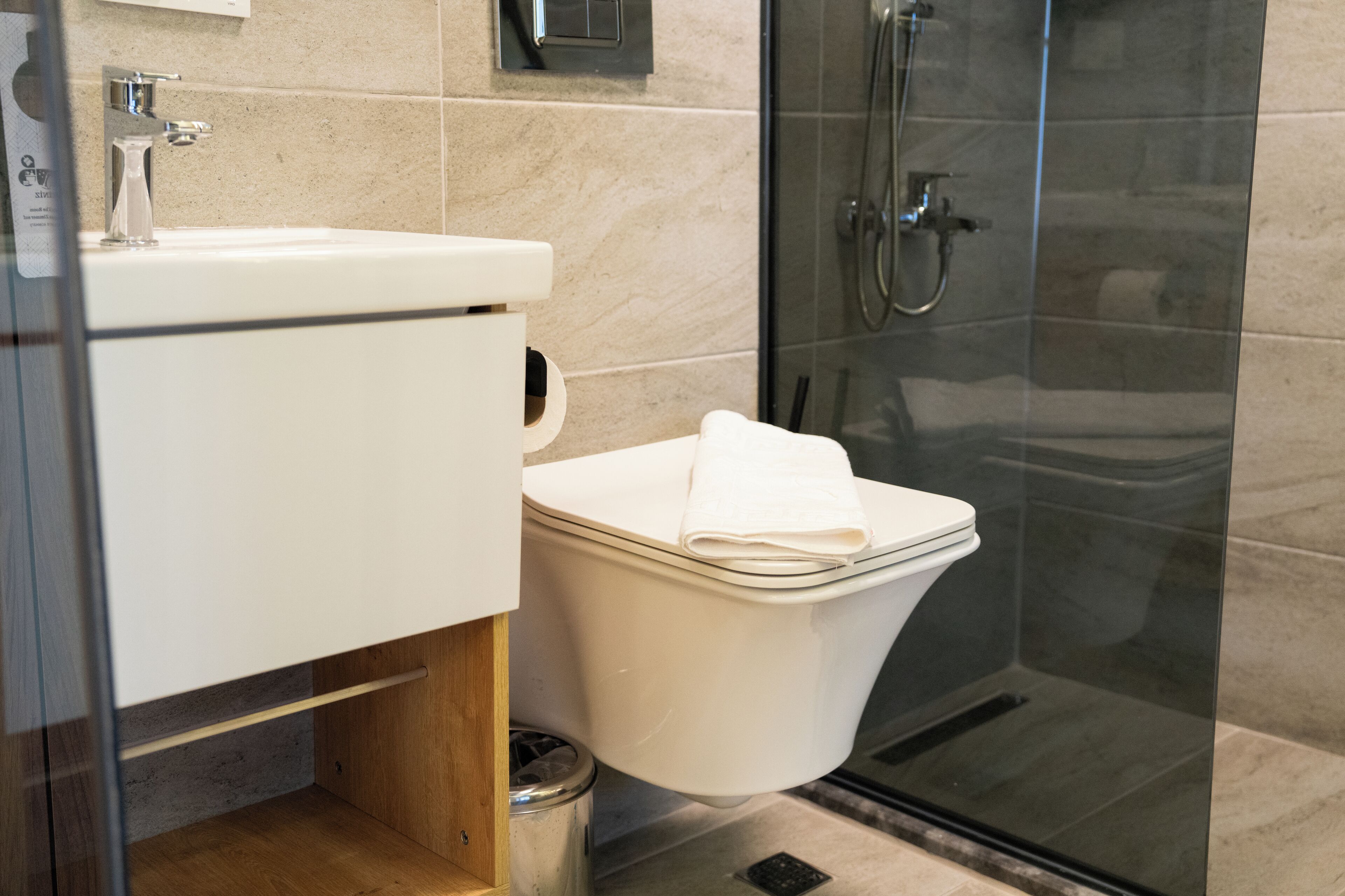 Een moderne badkamer met een douchecabine van glas, een witte wastafel en een toilet met een handdoek erboven.