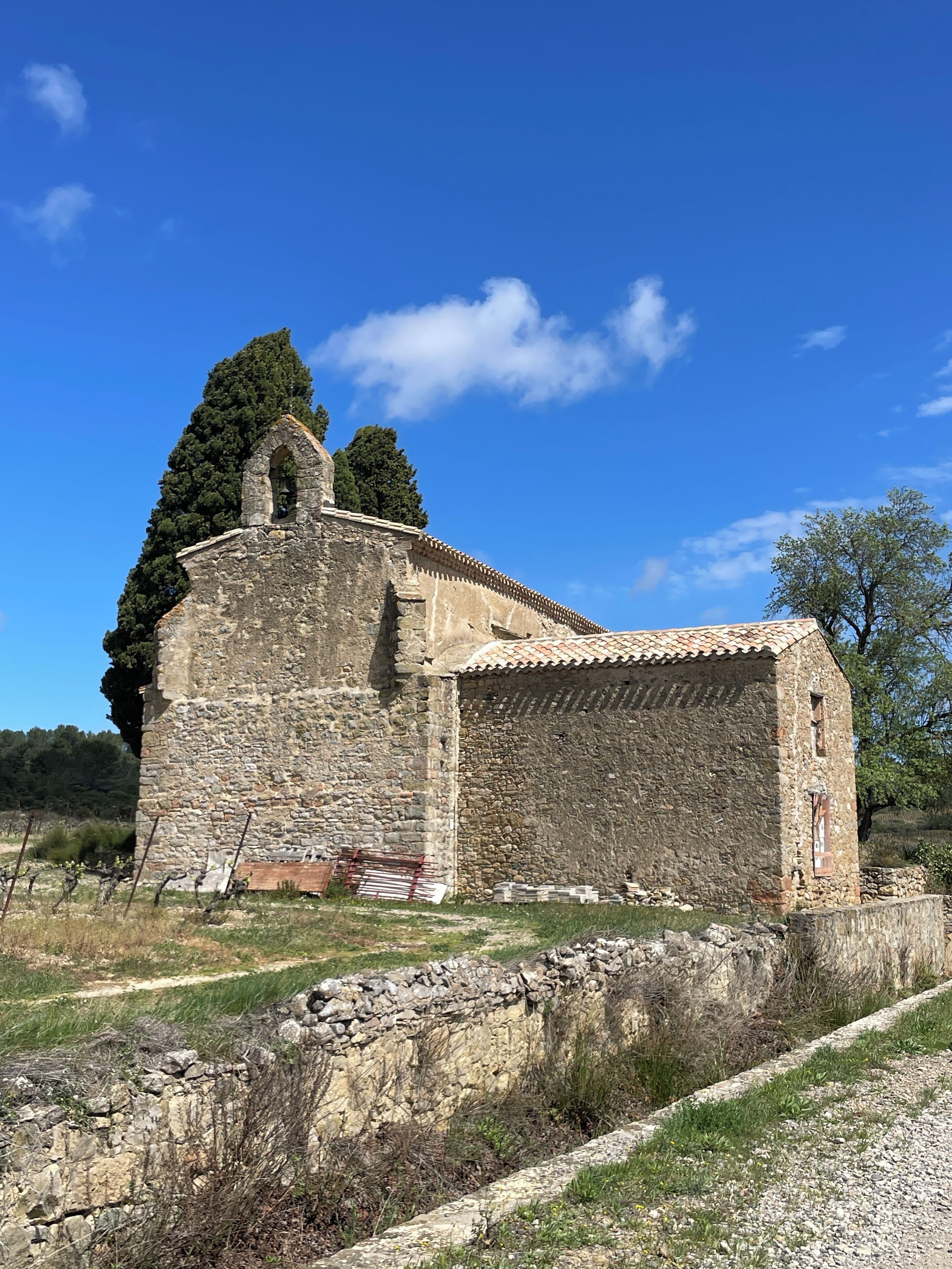 An ancient stone building with a bell tower, surrounded by trees and a clear blue sky.