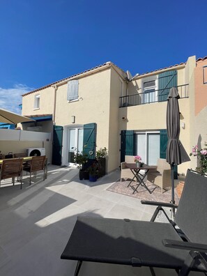 A two-story building with a patio area featuring outdoor furniture, a table, and potted plants.