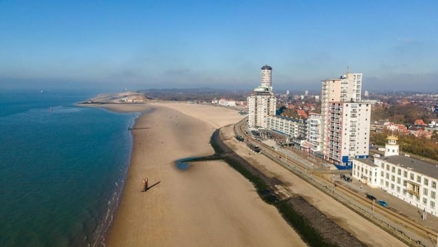 Un paysage urbain côtier avec une vaste plage de sable, de hauts immeubles et un ciel bleu dégagé.
