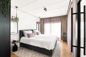 Ein modernes Schlafzimmer mit einem großen Bett, einem runden Beistelltisch und Blick ins Freie.