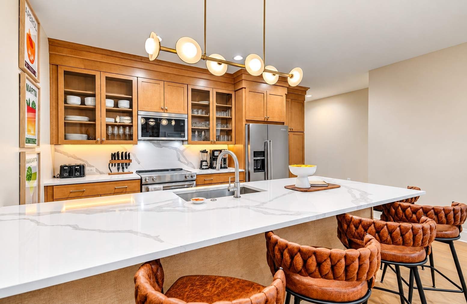 A modern kitchen with wooden cabinets, a central island, and leather bar stools.