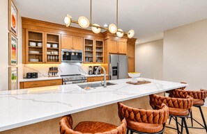 A modern kitchen with wooden cabinets, a central island, and leather bar stools. - Chic Nash Home, 4bd/4ba w/ Hot Tub & Rooftop! (Nashville)