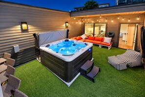A hot tub with a cover, surrounded by outdoor seating and a string of lights. - Chic Nash Home, 4bd/4ba w/ Hot Tub & Rooftop! (Nashville)