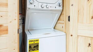 A compact laundry room with a stacked washer and dryer, wooden walls, and a visible energy efficiency label. - Black Butte - Lux Family Cabin With Games Firepit (Sevierville)