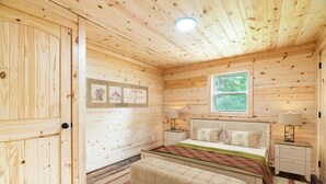 A wooden-paneled bedroom with a bed, bedside tables, a window, and framed pictures on the wall. - Black Butte - Lux Family Cabin With Games Firepit (Sevierville)