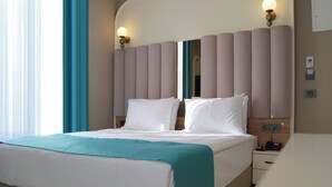 Een hotelkamer met een bed, nachtkastje, een wandlamp en een raam met gordijnen.