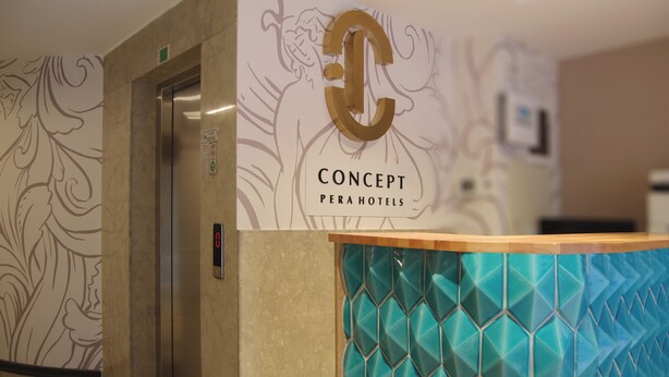 Een hotel receptie met een groot ‘C’ logo, een receptiebalie met een geometrisch tegelontwerp en een lift.