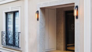 Een gevelingang met een trap die naar een deur leidt, een raam met een metalen balkon en twee wandlampen.