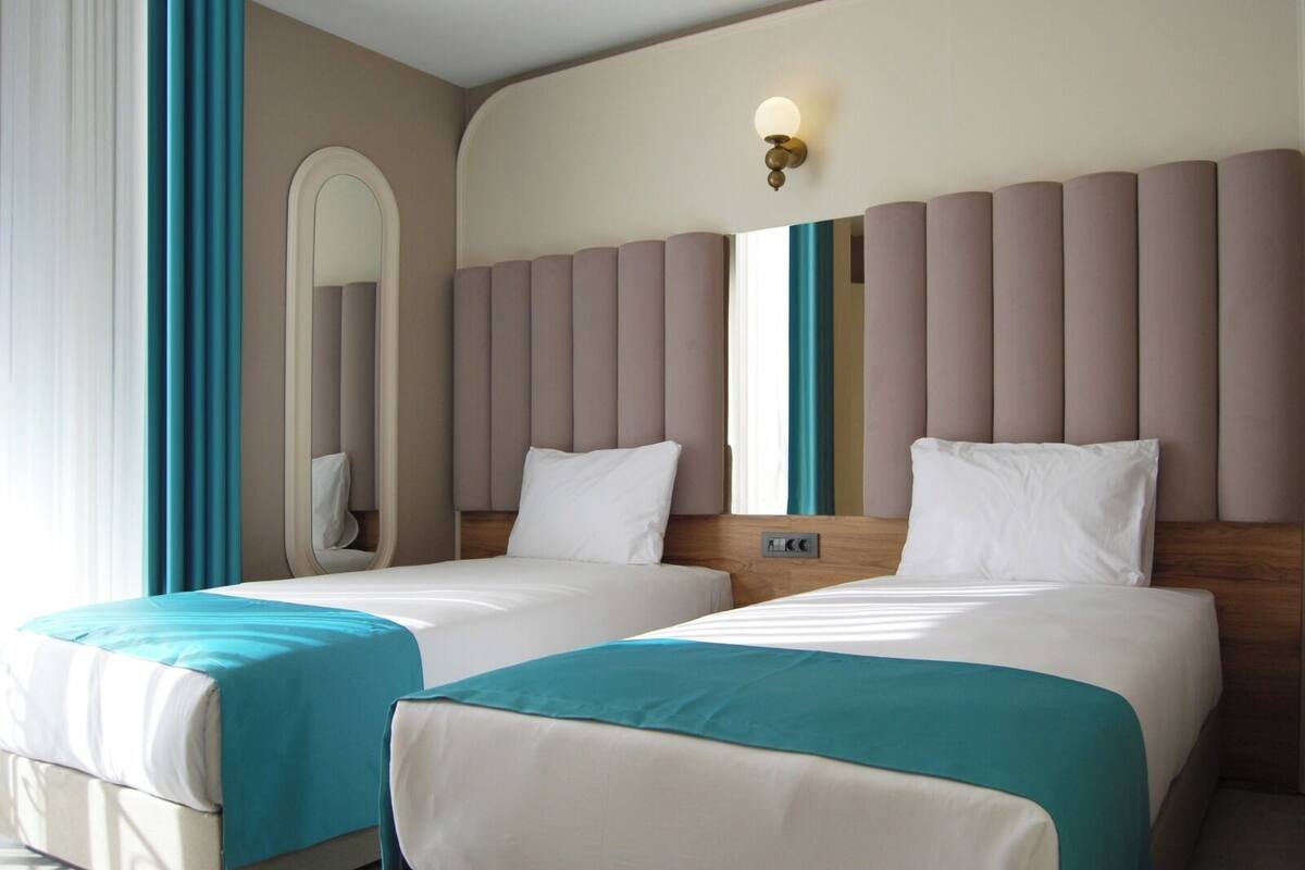 A hotel room with two beds, a large mirror, and a wall-mounted light fixture.