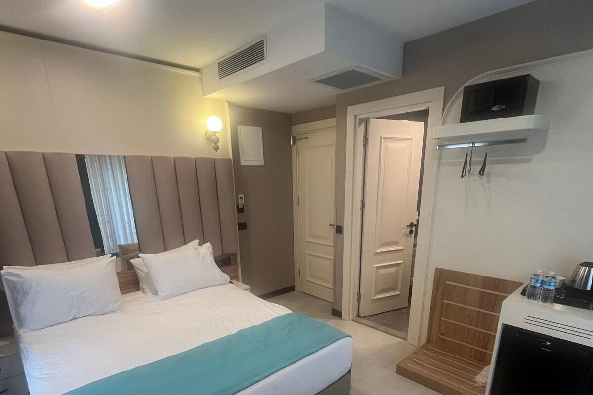 A hotel room with a large bed, a bedside table with a microwave, a wardrobe, and a door leading to another room.