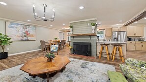A spacious living room with a wooden dining table, a fireplace, and a kitchen area with bar stools.
