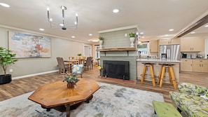 A spacious living room with a wooden dining table, a fireplace, and a kitchen area with bar stools.