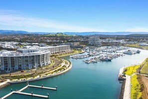 Un puerto deportivo con varias embarcaciones amarradas, rodeado de edificios modernos y una vista despejada de las colinas lejanas.