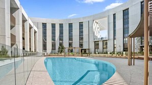 Un edificio moderno con una piscina grande, barandillas de vidrio transparente y un diseño curvo.