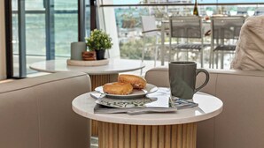 Un área de descanso moderna con una mesa redonda, un plato de rosquillas, una taza y un periódico.