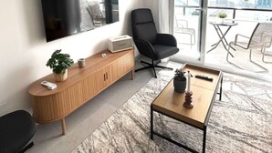 Un salón moderno con un televisor de pantalla plana, una silla negra, un mueble de madera y una mesa de centro.