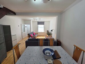 A dining area with a table set for two, a sofa, and a television in the background.