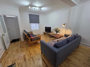 A living room with a sofa, a television, a coffee table, and a lamp.