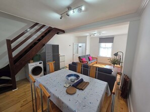 A dining area with a table set for two, a wooden chair, a ceiling light fixture, and a staircase.