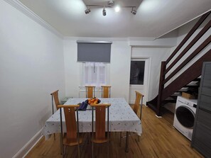 A dining area with a table and chairs, a window with a blind, a washing machine, and a staircase.