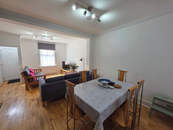 A modern living room with a dining table, sofas, a TV, and a window with curtains.