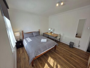 A bedroom with a bed, a desk, a chair, a lamp, a mirror, and a radiator.