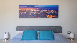 Un letto rifatto con precisione, con una testiera grigia, due cuscini blu e una vista sulla città sullo sfondo.