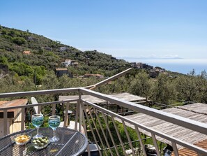 Une terrasse avec une table dressée pour deux personnes, donnant sur une colline parsemée de bâtiments et offrant une vue sur la mer.