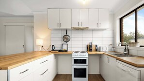 A modern kitchen with white cabinets, a wooden countertop, a stove, a sink, and a window.