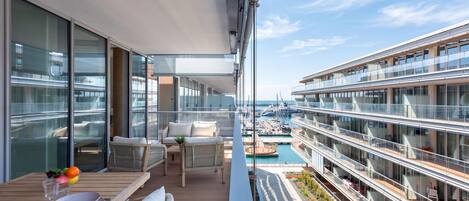 A modern balcony with outdoor furniture, a dining table, and a view of a marina with boats.
