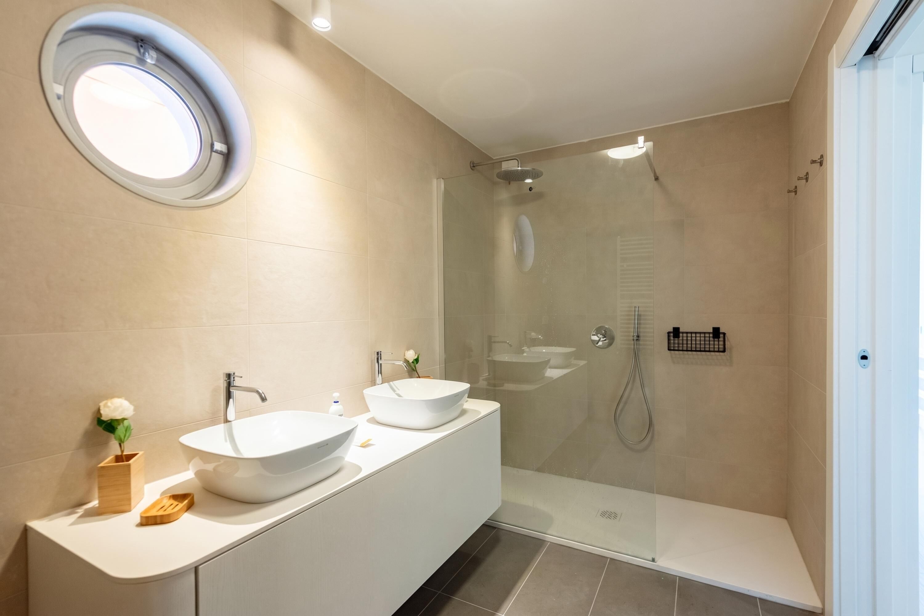 Un baño moderno con tocador doble, ducha con cerramiento de vidrio y espejo redondo.