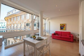 A modern living room with a red sofa, a dining table with chairs, and a large window overlooking a cityscape. - Genova House Historic Center (Genoa)