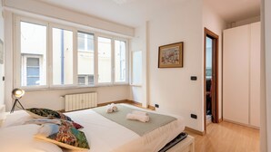 Een slaapkamer met een bed, een bedlampje, een raam, een schilderij en een kledingkast.