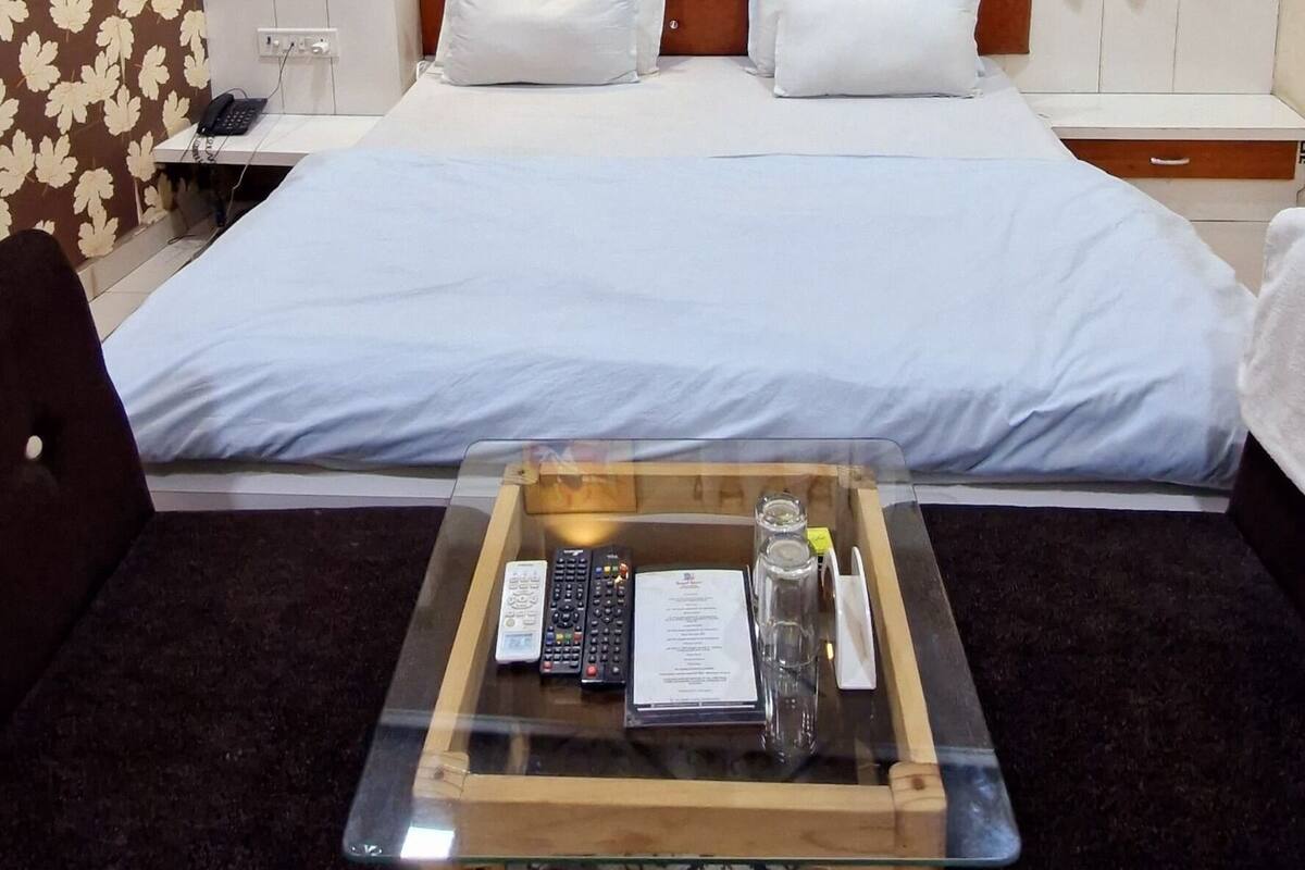 A hotel room with a bed, a small table with a tray, a ceiling fan, a window with curtains, and a wall with two framed pictures.