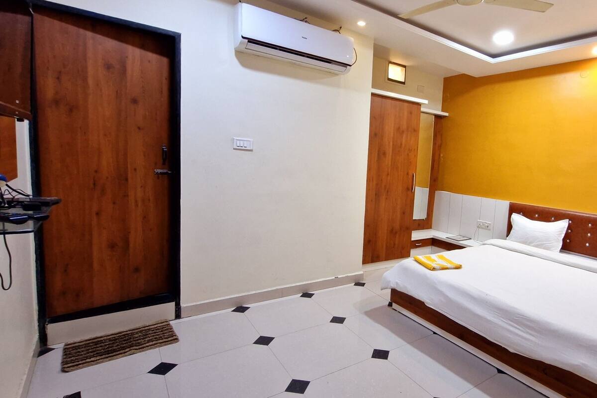 A hotel room with a bed, wooden wardrobe, air conditioning unit, and a bedside table.