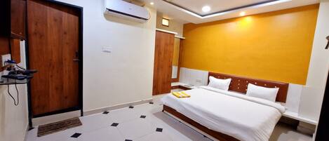 A hotel room with a bed, wooden wardrobe, air conditioning unit, and a bedside table.