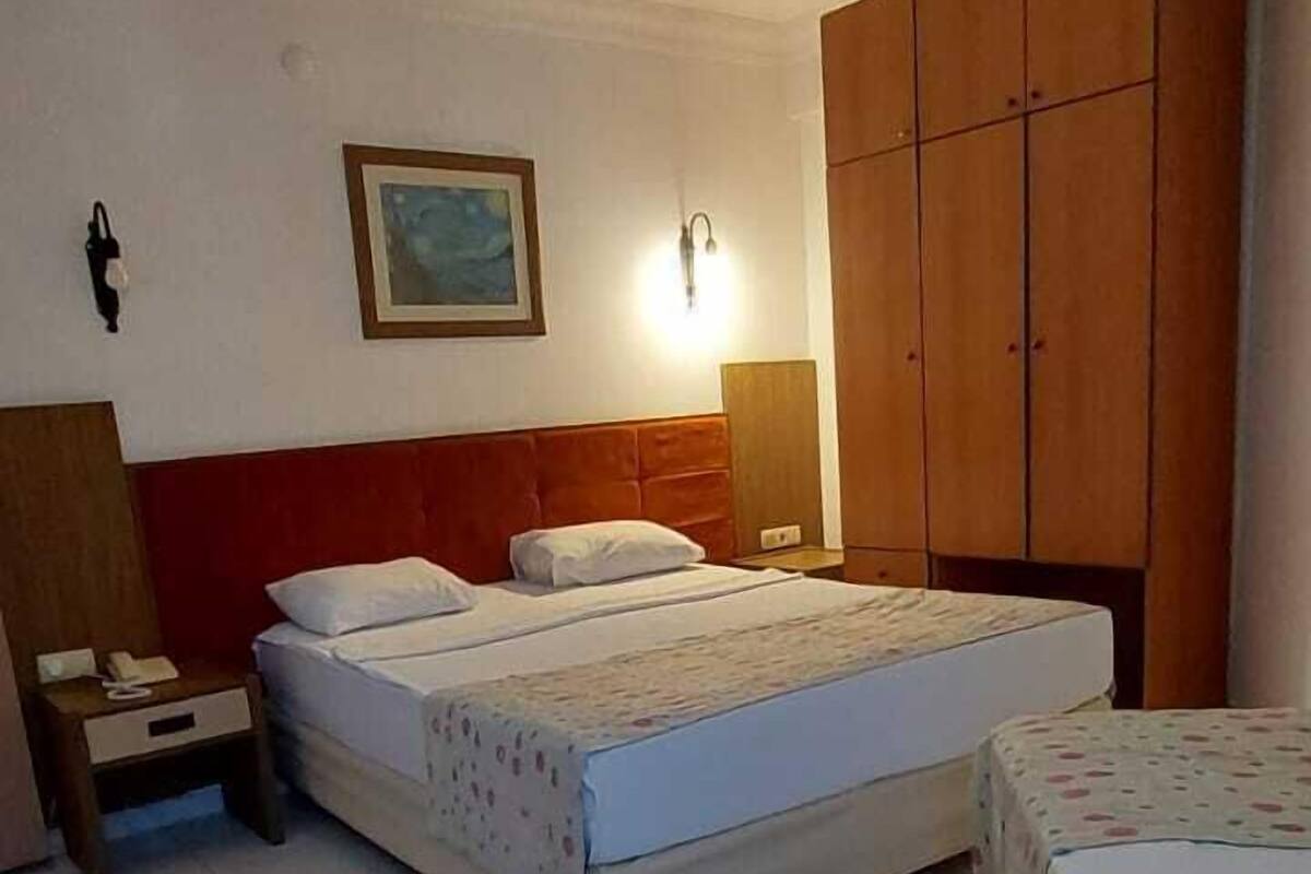Un dormitorio con dos camas, un armario de madera, una mesita de noche con una lámpara y un cuadro enmarcado en la pared.