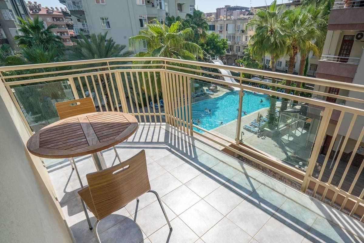 Un balcón con baranda de cristal, una piscina y una mesa con sillas.