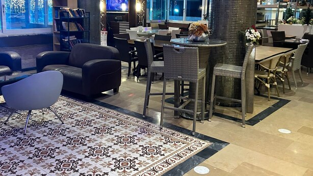 A modern lobby with a patterned carpet, seating areas, and a large pillar. - Kleopatra Carmen Apart (Alanya)