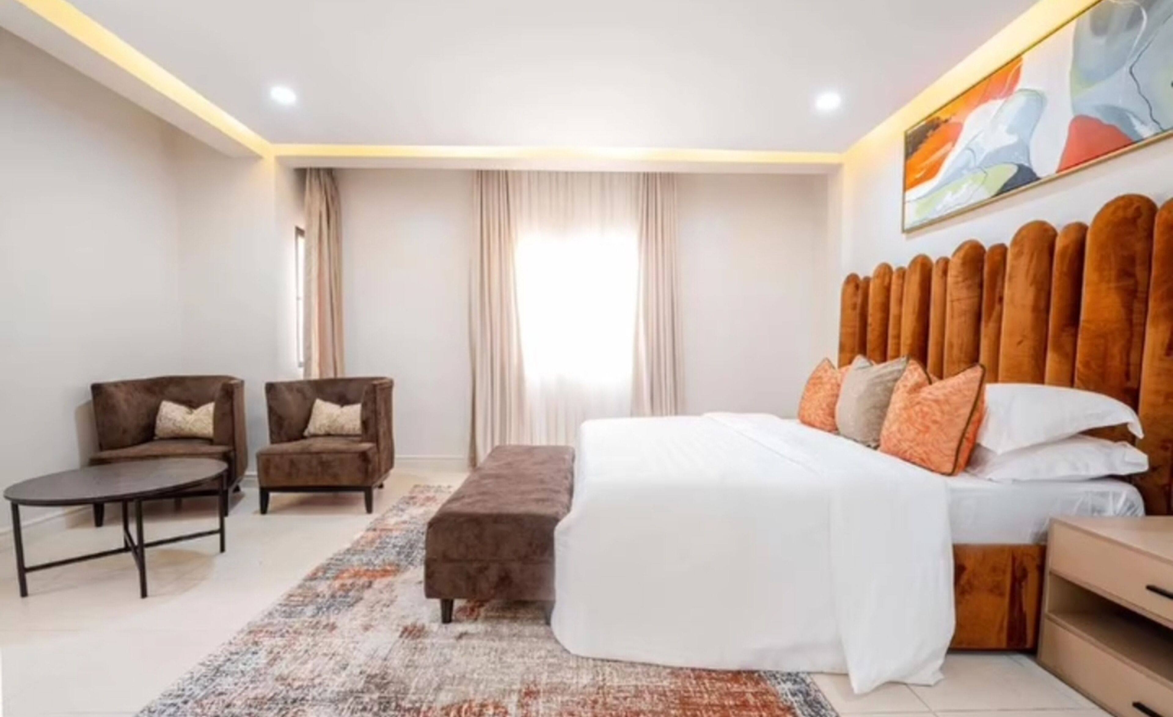 A bedroom with a bed, two armchairs, a small table, and a rug.