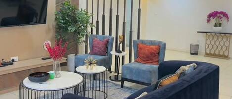 A modern living room with a sofa, two armchairs, a coffee table, and a TV mounted on the wall.