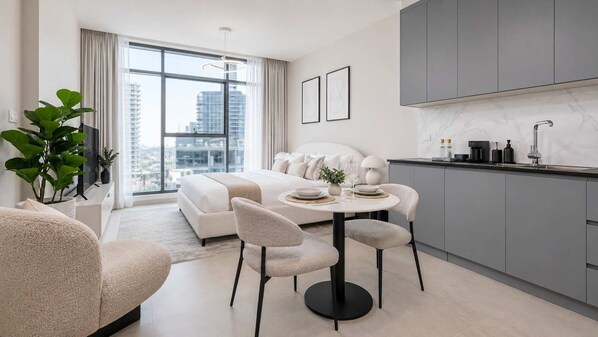 Un salon moderne avec un canapé, une table à manger et des chaises, une cuisine avec des meubles gris et une grande fenêtre donnant sur la ville.