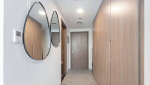 A hallway with a wooden wardrobe, a door, and a wall-mounted mirror. - StayShort - Stylish Modern Studio in Living Garden 2 (JVC)