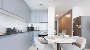 A modern kitchen with grey cabinets, a built-in stove, and a dining area with a round table and two chairs. - StayShort - Stylish Modern Studio in Living Garden 2 (JVC)