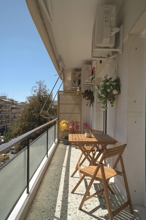 A balcony with a wooden table and chairs, potted plants, and hanging flower baskets. - Mixalakopoulou Luxury Apartment (Athens)