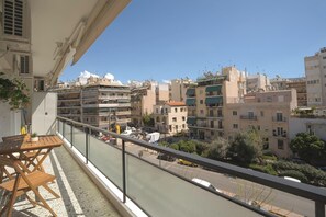 A balcony with a wooden table and chairs, overlooking a cityscape with multi-story buildings and a clear sky. - Mixalakopoulou Luxury Apartment (Athens)