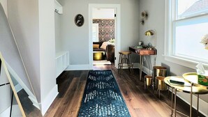 Un pasillo con piso de madera, un tapete azul oscuro, una escalera, un área de comedor con mesa y sillas, y un ventanal con vistas.